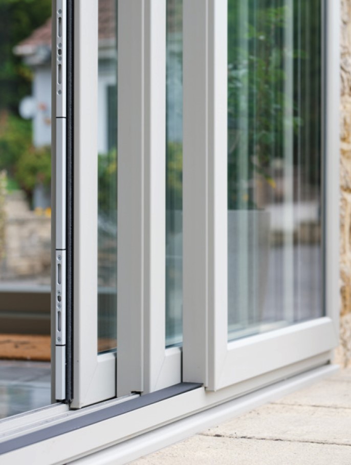 Close-up shot of a white modern triple track sliding patio door in a partially open position, highlighting the multi-point locking mechanism along the frame edge and the floor track.